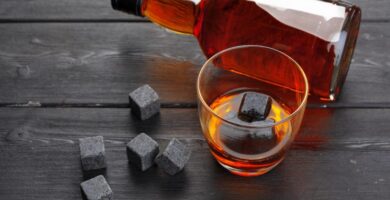 piedras de whysky stones con vaso y botella de whisky en mesa de madera